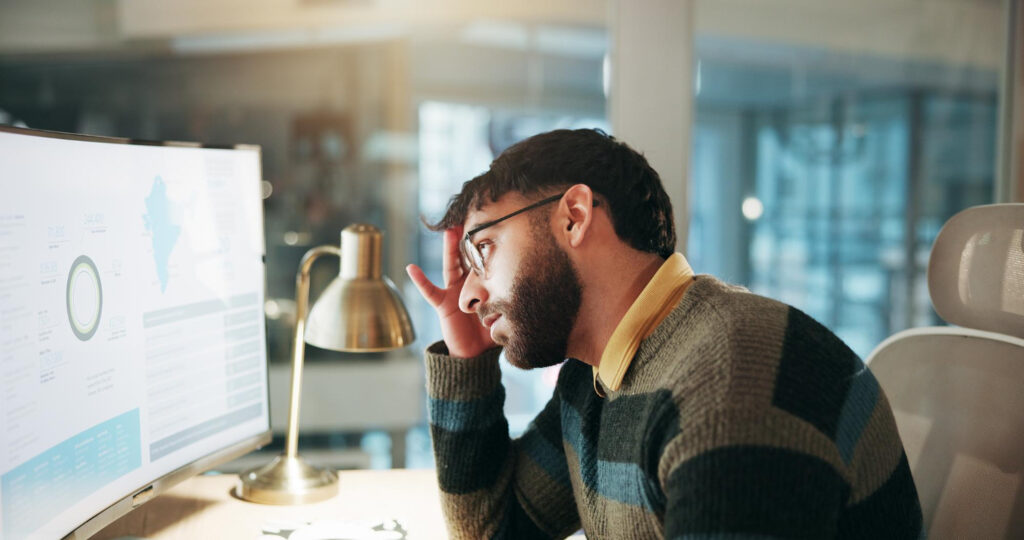 Man at a desk looking with concern at a monitor showing charts