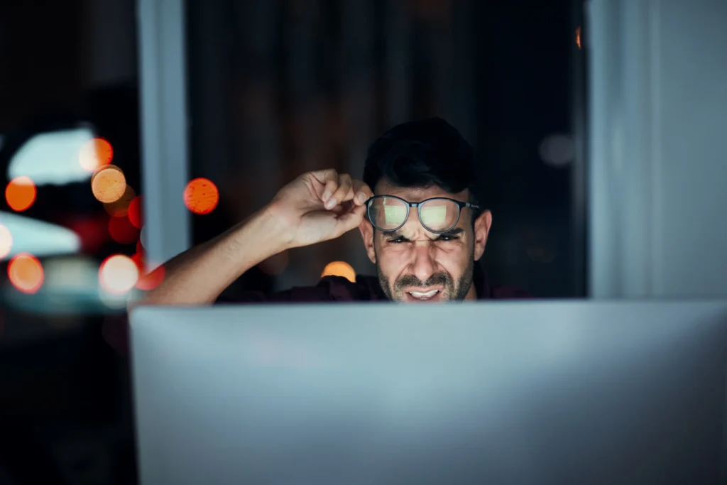 Man working late at night, his face lit by a laptop screen